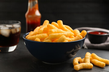 Bowl with crunchy cheesy corn snack on black table, closeup