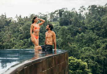 Wall Mural - Happy young couple relaxing at edge of swimming pool