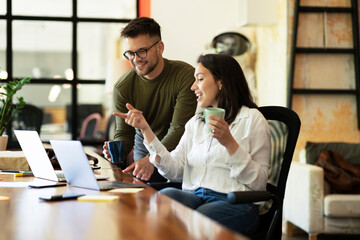 Wall Mural - Colleagues laughing in office. Businesswoman and businessman drinking coffee.