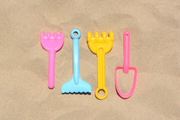 Wall Mural - Bright plastic rakes and shovel on sand, flat lay. Beach toys