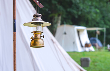 Wall Mural - Focus at the old vintage camping brass lantern with blurred background of white field tents in camping area at natural park