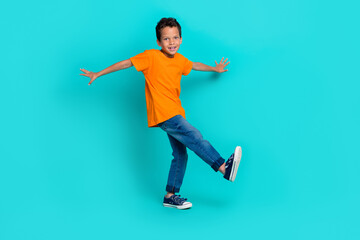 Poster - Full length photo of cheerful boy dressed trendy orange clothes stand one leg foot good mood empty space isolated on cyan color background