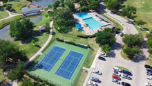 Aerial View Large Tennis Court And Swimming Pool At Community Recreational Center With Trails And Pond Near Dallas, Texas, USA. Green Park Surrounded By Mature Trees, Busy Parking Lots And Outdoors