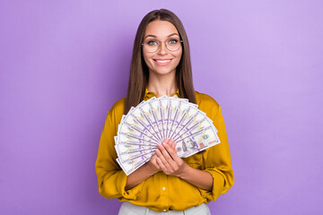 Wall Mural - Portrait of cheerful pretty girl hands hold dollars banknotes bills isolated on purple color background