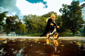 Cutie little girl rides through the puddles on bicycle at the park