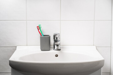 Toot brush cup in bathroom and toilet sink. Toothbrush in clean restroom. Water tap, faucet and basin to wash hands in WC. Glass jar. Dental hygiene and home washroom design concept. Family apartment.