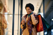 © Drazen - Happy black woman texting on cell phone while shopping in city.
