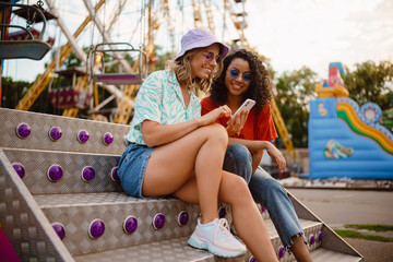 Wall Mural - Young multiracial women using cellphone in attraction park