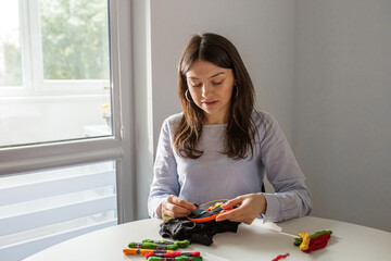 Wall Mural - Woman cross-stitches, sitting by window. Hobby of young adult girl.