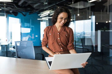 Wall Mural - Young beautiful business woman working with laptop smiling and happy, Hispanic woman inside modern office building wearing glasses and curly hair.