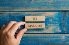 Male Hand Assembling A We Apologize Sign Written On Two Wooden Pegs
