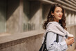 © Look! - Beautiful young caucasian woman with coffee looking at camera spending time on break from work. Brunette with wavy hair wears shirt, sweatshirt and bag. Lifestyle concept