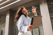 © Look! - Happy young caucasian woman winking and showing ok gesture at camera standing on street. Brunette uses modern devices. Work business concept