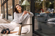 © Look! - Pretty young caucasian brunette woman posing looking at camera sitting outdoors. Model wears light-colored casual clothes in spring. City life concept
