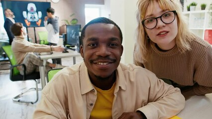 Caucasian woman and African American man discusses something and looks at the camera as if in a monitor in an office for the development of games and computer applications.