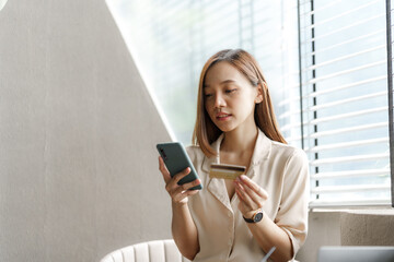 Young pretty asian female using credit card to do online product shopping on her mobile, cashless concept.