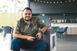 © JulianSarmiento - portrait of a dark-haired man, sitting in a cozy space. Young Colombian sitting in a shopping mall, sharing a moment. latin american person in a casual pose