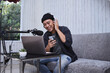 © Gatot - Asian man making a podcast from home studio while holding smartphone. Recording a podcast for online channel.