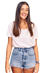 Wall Mural - Young hispanic woman wearing casual white tshirt winking looking at the camera with sexy expression, cheerful and happy face.