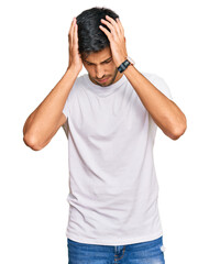 Young handsome man wearing casual white tshirt suffering from headache desperate and stressed because pain and migraine. hands on head.