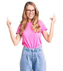 Canvas Print - Young beautiful caucasian woman with blond hair wearing casual clothes and glasses shouting with crazy expression doing rock symbol with hands up. music star. heavy concept.