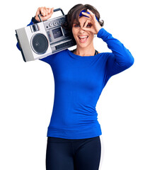 Wall Mural - Beautiful young woman with short hair wearing workout clothes and holding boombox smiling happy doing ok sign with hand on eye looking through fingers