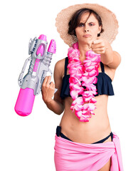 Wall Mural - Beautiful young woman with short hair wearing bikini and hawaiian lei holding water gun pointing with finger to the camera and to you, confident gesture looking serious