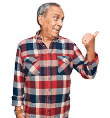 Canvas Print - Senior hispanic man wearing casual clothes smiling with happy face looking and pointing to the side with thumb up.