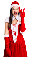 Sticker - Young beautiful caucasian woman wearing santa claus costume smiling with happy face winking at the camera doing victory sign with fingers. number two.