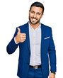 © Krakenimages.com - Young hispanic man wearing business jacket doing happy thumbs up gesture with hand. approving expression looking at the camera showing success.