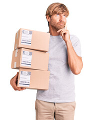 Poster - Handsome caucasian man with beard holding delivery packages serious face thinking about question with hand on chin, thoughtful about confusing idea