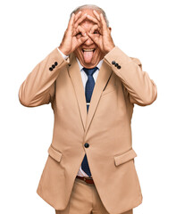 Canvas Print - Senior caucasian man wearing business suit and tie doing ok gesture like binoculars sticking tongue out, eyes looking through fingers. crazy expression.