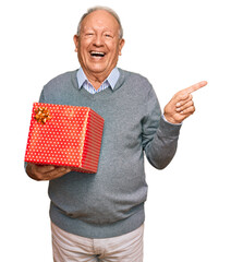 Canvas Print - Senior caucasian man holding gift smiling happy pointing with hand and finger to the side