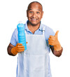© Krakenimages.com - Hispanic middle age man wearing cleaner apron holding cleaning products smiling happy and positive, thumb up doing excellent and approval sign