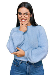 Wall Mural - Young hispanic woman wearing casual clothes and glasses looking confident at the camera smiling with crossed arms and hand raised on chin. thinking positive.