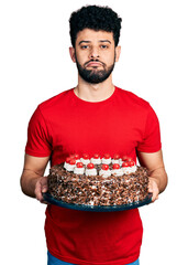 Poster - Young arab man with beard celebrating birthday holding big chocolate cake depressed and worry for distress, crying angry and afraid. sad expression.