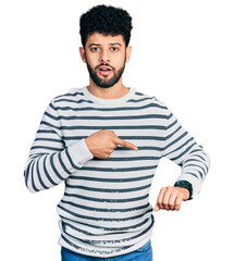 Canvas Print - Young arab man with beard wearing casual striped sweater in hurry pointing to watch time, impatience, upset and angry for deadline delay