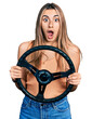 © Krakenimages.com - Hispanic young woman holding steering wheel afraid and shocked with surprise and amazed expression, fear and excited face.