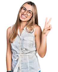 Wall Mural - Hispanic young woman wearing casual white shirt smiling with happy face winking at the camera doing victory sign. number two.