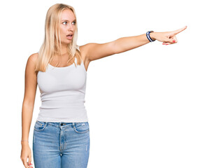 Wall Mural - Young blonde girl wearing casual style with sleeveless shirt pointing with finger surprised ahead, open mouth amazed expression, something on the front