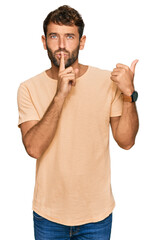 Poster - Handsome young man with beard wearing casual tshirt asking to be quiet with finger on lips pointing with hand to the side. silence and secret concept.