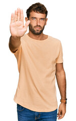 Poster - Handsome young man with beard wearing casual tshirt doing stop sing with palm of the hand. warning expression with negative and serious gesture on the face.