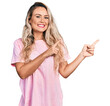© Krakenimages.com - Young blonde woman wearing casual pink t shirt smiling and looking at the camera pointing with two hands and fingers to the side.