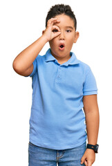 Wall Mural - Little boy hispanic kid wearing casual clothes doing ok gesture shocked with surprised face, eye looking through fingers. unbelieving expression.