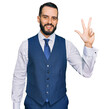 © Krakenimages.com - Young man with beard wearing business vest showing and pointing up with fingers number three while smiling confident and happy.