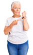 Senior beautiful woman with blue eyes and grey hair wearing casual white tshirt in hurry pointing to watch time, impatience, looking at the camera with relaxed expression