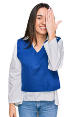 Poster - Young hispanic girl wearing casual clothes covering one eye with hand, confident smile on face and surprise emotion.