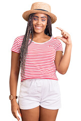 Sticker - Young african american woman with braids wearing summer hat smiling and confident gesturing with hand doing small size sign with fingers looking and the camera. measure concept.