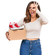 © Krakenimages.com - Young brunette woman holding box with red casual shoes smiling happy doing ok sign with hand on eye looking through fingers