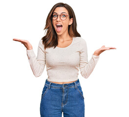 Wall Mural - Young brunette woman wearing casual clothes and glasses celebrating crazy and amazed for success with arms raised and open eyes screaming excited. winner concept